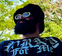 Nevv Evve wearing a black bucket hat and white sunglasses outdoors, looking upward beneath green trees, representing upcoming music releases and future projects.