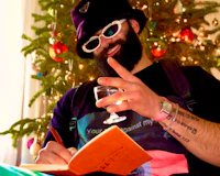 Nevv Evve brainstorming melody and lyric ideas over the holidays during a personalized creative session with his notebook and a glass while wearing a Prada bucket hat and artist luxury accessories.